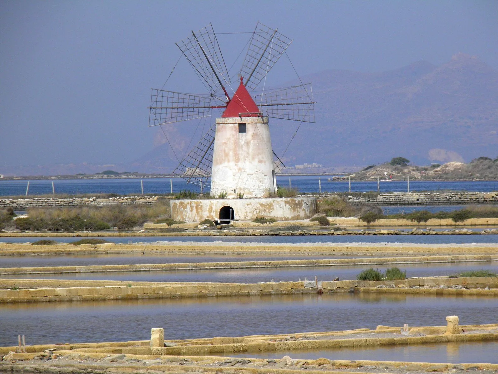 Mulino a vento con tetto rosso tra le vasche delle saline di Trapani